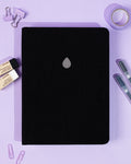 Black notebook with a silver logo on a purple background with stationery items.